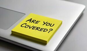 Homeowners reviewing an insurance policy beside a folder, camera, receipts, and a household inventory checklist.