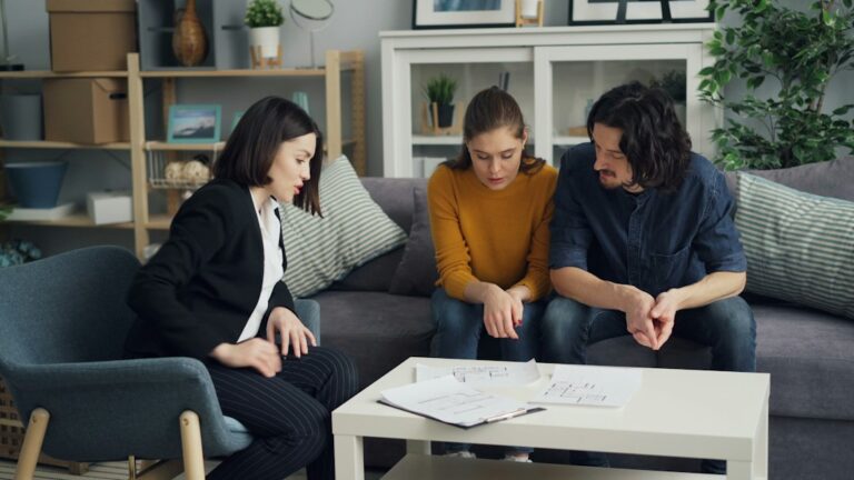 Two people review repair estimates and photographs beside a storm-damaged home.